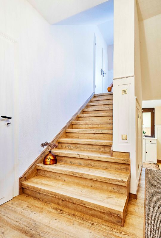 Holzstruktur, die man sehen und spüren kann: Diese Treppenverkleidung aus Vinyl und die halbhohe Wandvertäfelung sorgen im Zusammenspiel für einen elegenaten Landhaus-Stil.